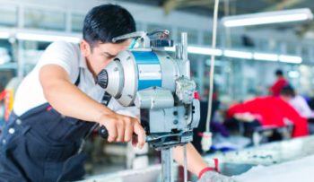 Indonesian worker using a cutter - a large machine for cutting fabrics - in a asian textile factory, he wears a chain glove